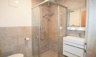 A modern bathroom with a glass shower and a white sink. The walls are in neutral brown and beige tones.