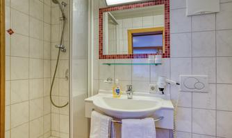 A modern bathroom with a shower and sink. The walls are tiled white, and there is a large mirror.